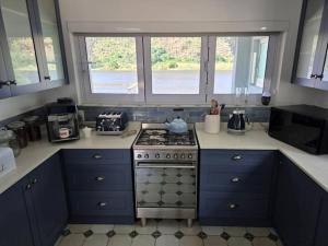 a kitchen with blue cabinets and a stove and two windows at Jonker's Cottage in Malgas +14 photos