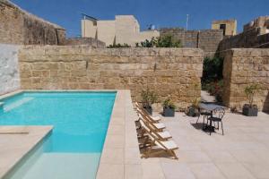a swimming pool with lounge chairs next to a stone wall at Lemon Tree Relais by CX Collection in Żabbar