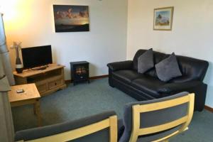 a living room with a black leather couch and a television at Wheal Rodney Holiday Park in Marazion