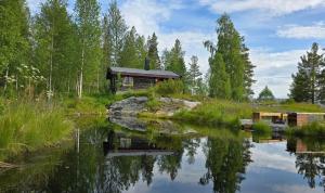 a log cabin next to a river with trees at Smia cabin , A Unique Rustic Hideaway in Lii