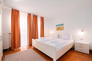a white bed in a bedroom with orange curtains at Strandhaus Lobbe, Sanddorn Nr 3 - Bade- & Saunawelt täglich inklusive in Lobbe