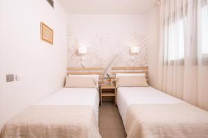 two beds in a room with white walls and windows at Apartamentos Castellmar in Castelldefels
