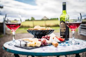 a table with two glasses of wine and a plate of food at The Swift, Shepherds Hut at Bee Happy Breaks Scotland in Perth