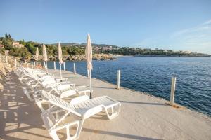 a row of white chairs and umbrellas next to the water at Aleksandra Apartments Utjeha in Utjeha