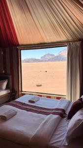 a bed in a tent with a large window at Wadi rum camp in Wadi Rum