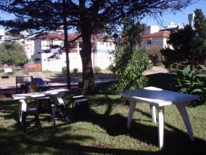 two white picnic tables and chairs under a tree at Hostal Sur in Villa Gesell