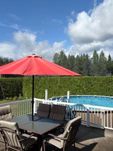 ein Tisch mit einem roten Sonnenschirm neben einem Pool in der Unterkunft Chalet St-Côme in Saint Come
