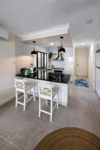 a kitchen with a black counter top and white chairs at La Plage Cabane in Eimeo