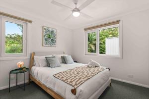 a white bedroom with a bed and two windows at Blenheim Breeze by Experience Jervis Bay in Vincentia
