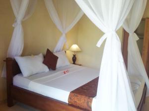 a bedroom with a bed with white curtains at Molleh Guest House in Pemuteran