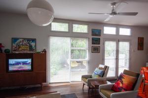 a living room with two chairs and a tv and windows at Eco Retro Aldinga Beach House in Aldinga Beach