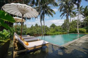 a resort pool with lounge chairs and an umbrella at Pertiwi Bisma 1 in Ubud