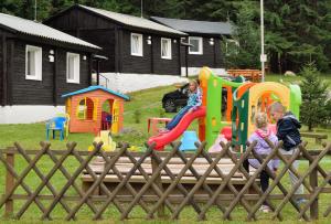 zwei Kinder spielen auf einem Spielplatz hinter einem Zaun in der Unterkunft Chaty Jasná in Demänovská Dolina