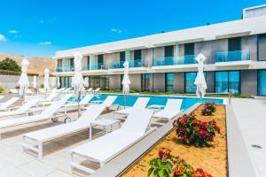 a pool at the hotel with white lounge chairs and umbrellas at Vila Baleira Village in Porto Santo