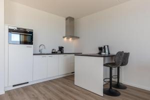 a kitchen with white cabinets and a bar stool at Welcome in - Royaal appartement 'De Zeester' met riant terras I Gorishoeksedijk 41, Scherpenisse in Scherpenisse