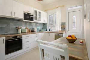 a kitchen with white cabinets and a table with a bowl of fruit at Athenais Two Storey House in Zakynthos +39 photos