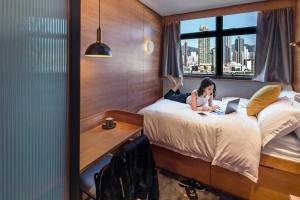 a girl laying on a bed in a hotel room with a laptop at Oootopia Kai Tak in Hong Kong