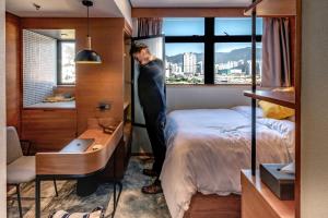 a man standing in a bedroom with a bed and a window at Oootopia Kai Tak in Hong Kong