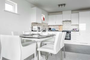 a white kitchen with a table and white chairs at Beach Point - Stunning Harbour Views from Balcony in Poole