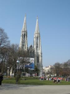 a cathedral with two towers with people sitting in the grass at Pension Schottentor in Vienna
