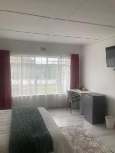 a bedroom with a bed and a desk and a window at Rio Lodge in Butterworth