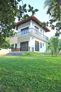 a white house with a large lawn in front of it at Cormorant Bath in Netolpitiya