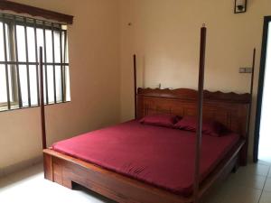 a bedroom with a wooden bed with a red bedspread at Mariagletta Cozy Villa in Abomey-Calavi