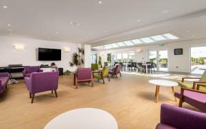 a waiting room with purple chairs and tables and a tv at Maison des Landes - Accessible Hotel in St. Ouen's