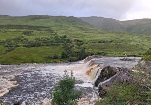 a river in the middle of a field with mountains at Wooly Lodge in Westport