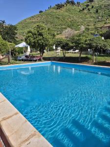 a blue swimming pool with a hill in the background at Villa Rica in Patti