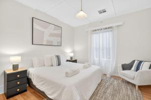 a white bedroom with a bed and a chair at The Wharf House Goolwa in Goolwa