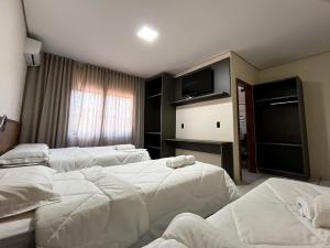a hotel room with three beds and a television at Hotel Rota 090 in Piraí do Sul