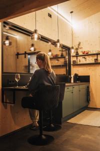 a woman sitting at a table in a kitchen at Rusty Cabin -Tiny House in Neustift an der Lafnitz