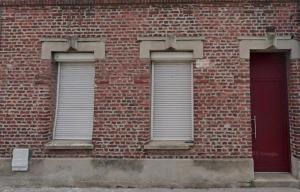 a brick building with two windows and a red door at T2 Elegant Super Centre in Beauvais