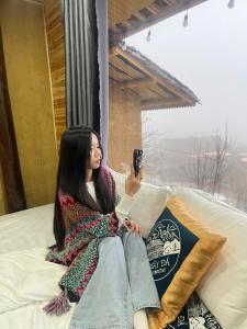 a woman sitting on a bed taking a picture with her cell phone at Mây Đá Homestay in Loung Co