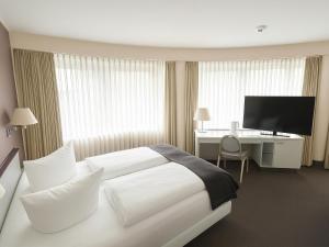 a hotel room with a bed and a desk with a television at DORMERO Hotel Dessau-Roßlau in Dessau