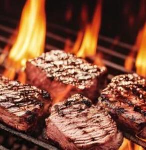 a group of steak cooking on a grill with flames at Hostal Boutique Restaurante El Algars in Caseras