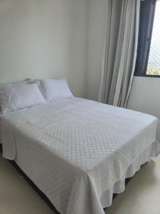 a white bed with a white comforter and a window at Beira Mar Apartment Aracaju in Aracaju