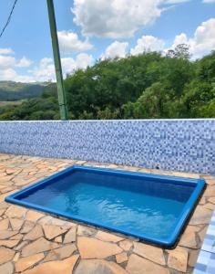 a blue swimming pool on a patio with a stone wall at Sítio encantador com piscina e lazer completo in São Roque