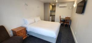 a small bedroom with a white bed and a chair at Waikato Hospital Motel in Hamilton
