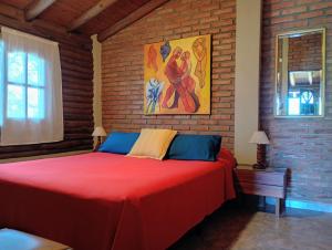 a bedroom with a red bed and a brick wall at Cabaña de troncos en Nono, Córdoba in Nono