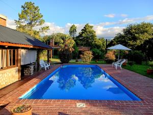 a swimming pool in a yard with two chairs and an umbrella at Cabaña de troncos en Nono, Córdoba in Nono