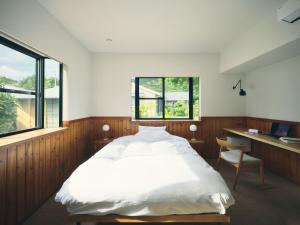 a bedroom with a bed and a desk and windows at SANU 2nd Home MON Amami Oshima in Tatsugo