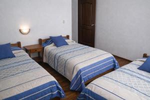 three beds in a room with blue and white sheets at Hostal Arias in Oxapampa