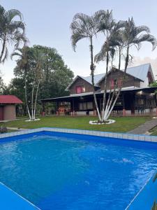 a blue swimming pool in front of a house with palm trees at Cabaña Brisa Del Río in Cooper