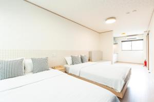 two beds in a room with white walls at air駅前民泊 in Izumi-Sano