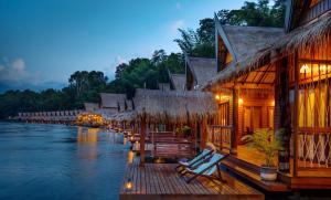 a river with a row of buildings and chairs on a dock at The Float House River Kwai in Sai Yok +28 photos
