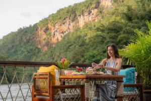a woman sitting at a table with a plate of food at The Float House River Kwai in Sai Yok