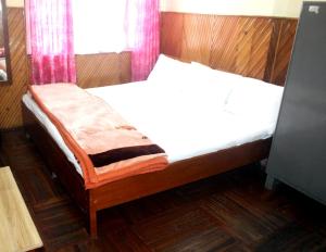 a bedroom with a bed with white sheets and pink curtains at Hotel Lhakhar in Gangtok