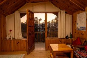 a living room with a large window and a table at Ishan Log Huts-A boutique home stay in Banjār